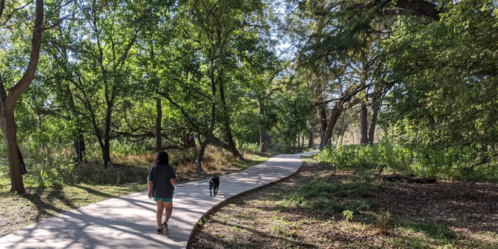 Two people walking along a paved trail with trees surrounding