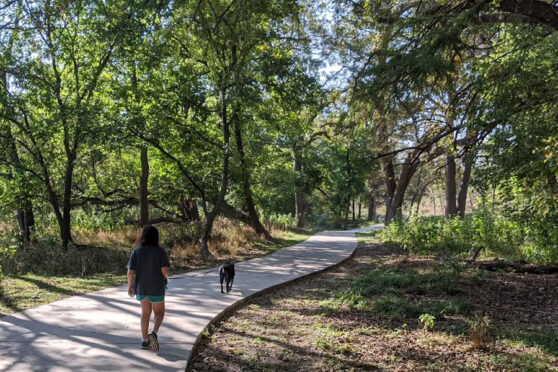 Two people walking along a paved trail with trees surrounding