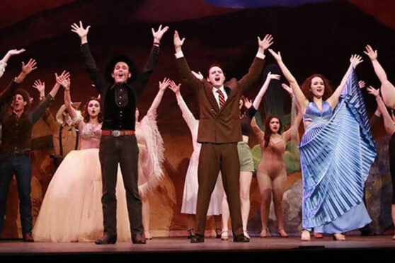 Actors with hands raised on stage after performance