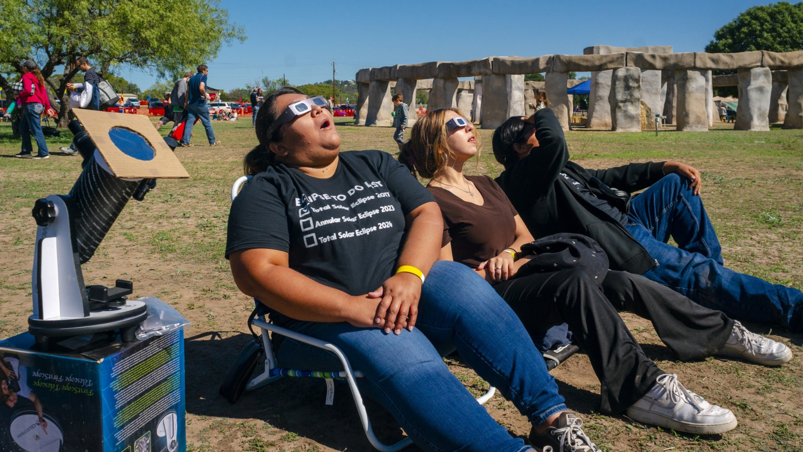 3 people in chairs looking at the solar eclipse with solar glasses