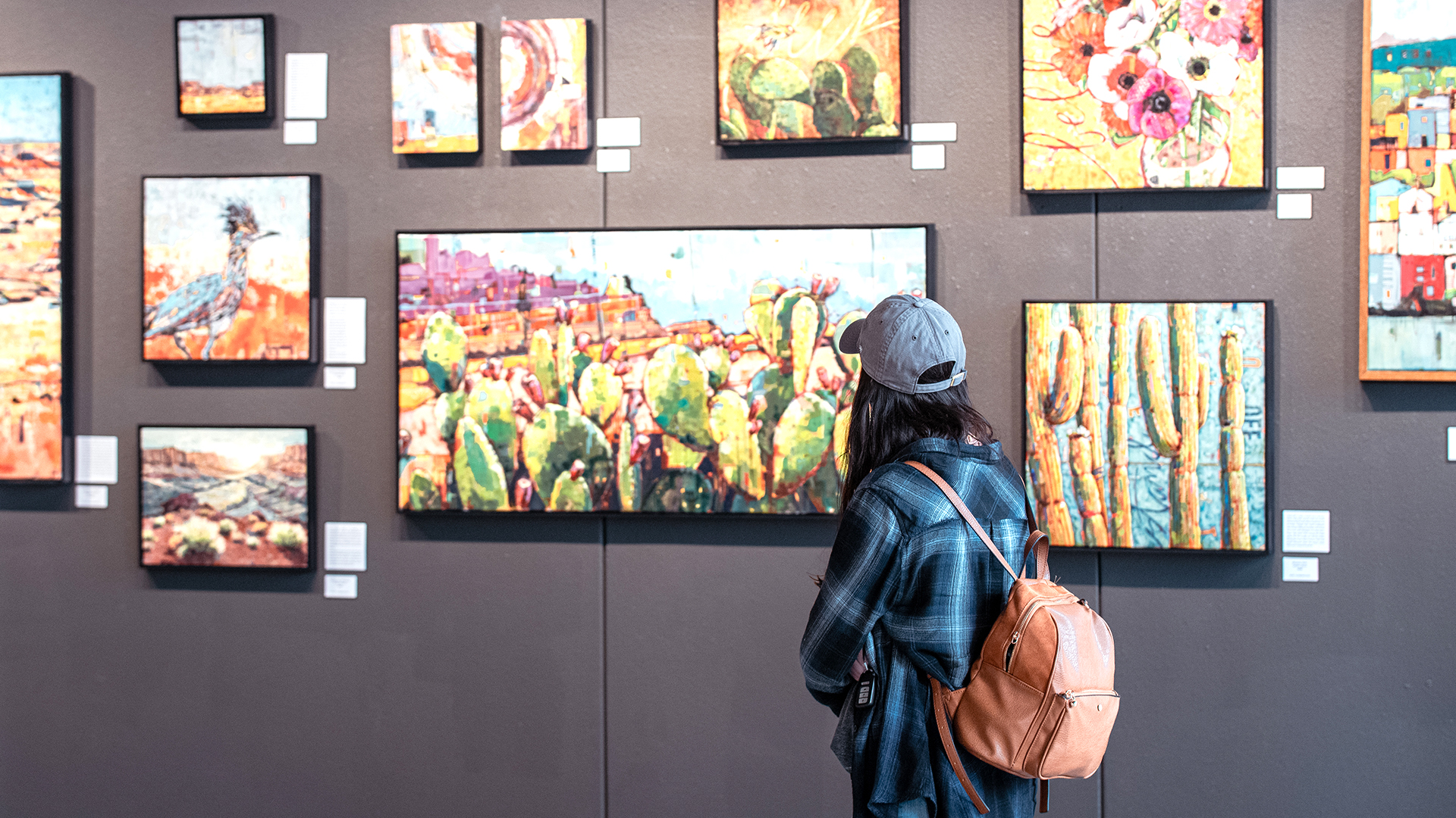 Woman in hat and backpack looking at art on the walls of a museum