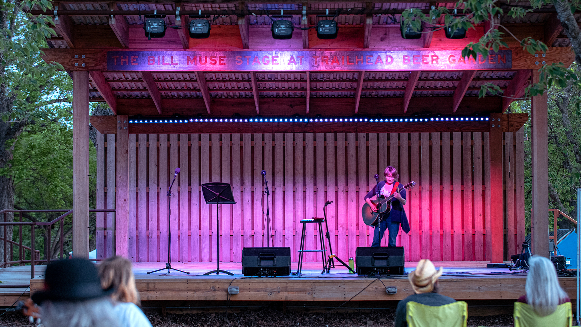 Woman with guitar performing on a stage with pink stage lights