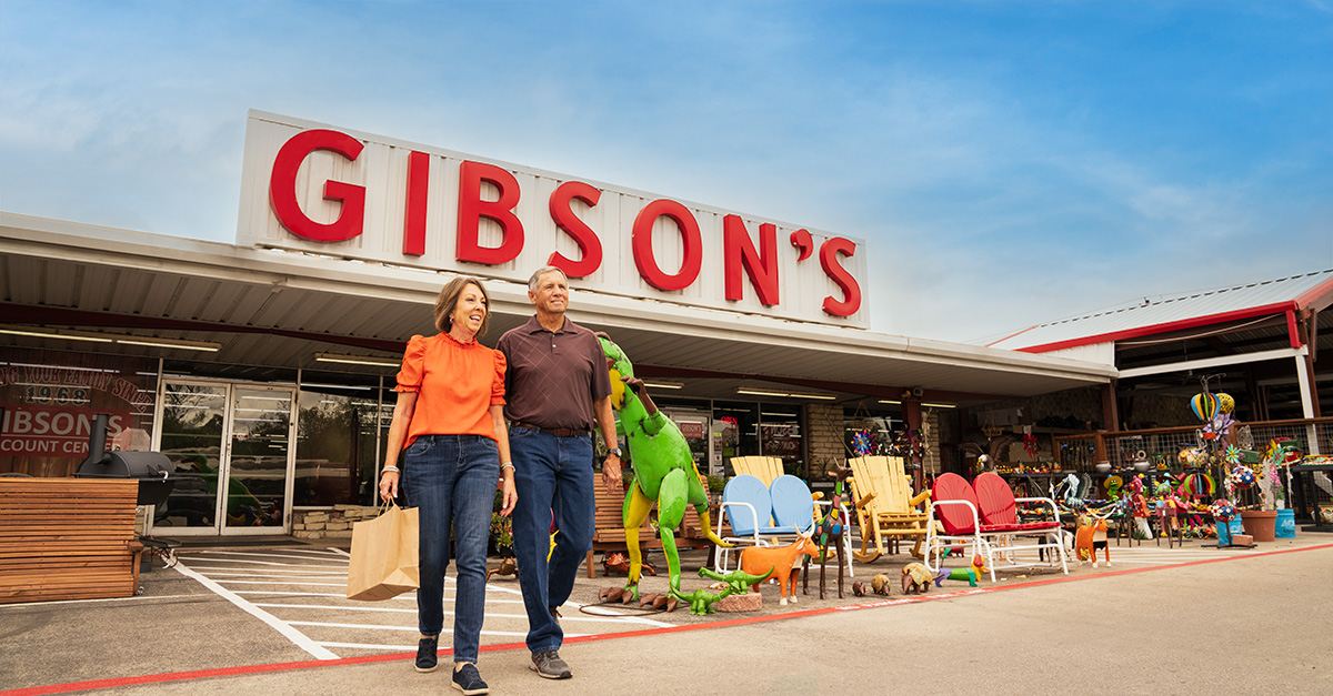Older couple walking in front of Gibson's Discount Store with merchandise for sale on the front patio of the store