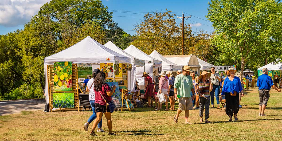 People walking in front of tents in a field at a festival or event