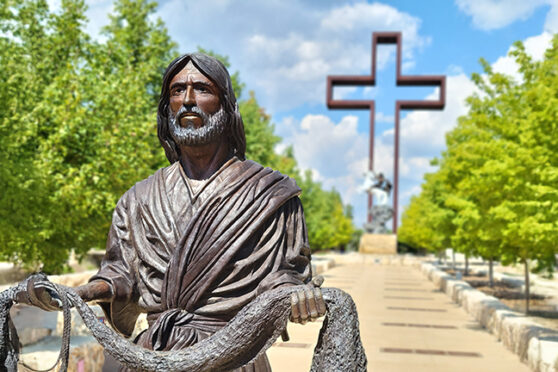 Statue of Jesus holding a fishing net in front of a large metal lifesize cross statue