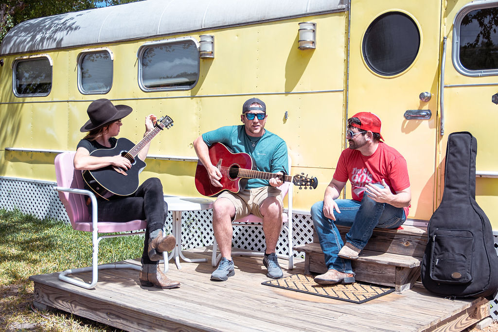 Group sitting in front of a yellow airstream trailer holding guitars and hanging out