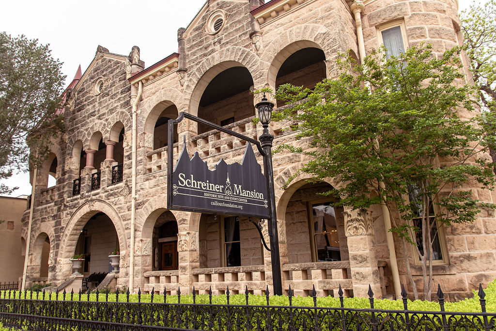 Front of Schreiner Museum in downtown Kerrville with sign and shrubs along fencing
