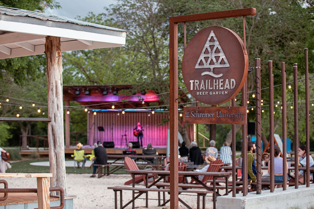 Person playing guitar on live stage at Trailhead Beer Garden with tables and hanging lights