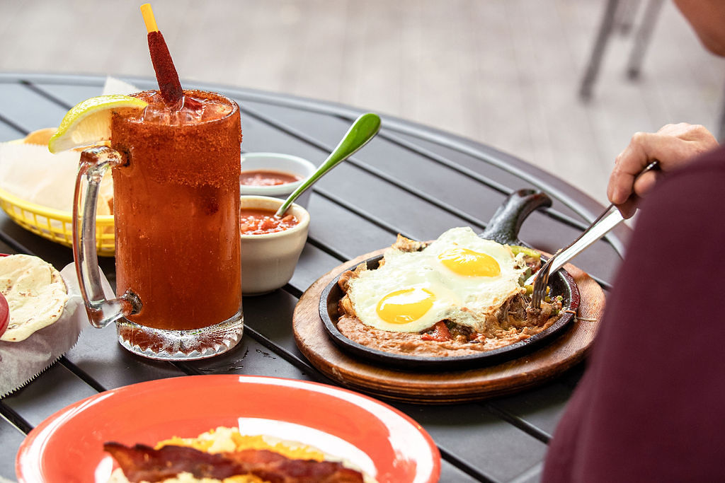 Tex Mex breakfast on an outdoor patio with enchiladas and eggs on a hot plat with a michelada to drink and side salsa
