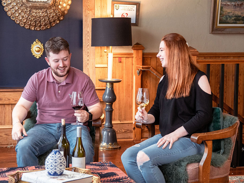 Young couple in chairs of cozy sitting area holding wine glasses with smiles on their faces