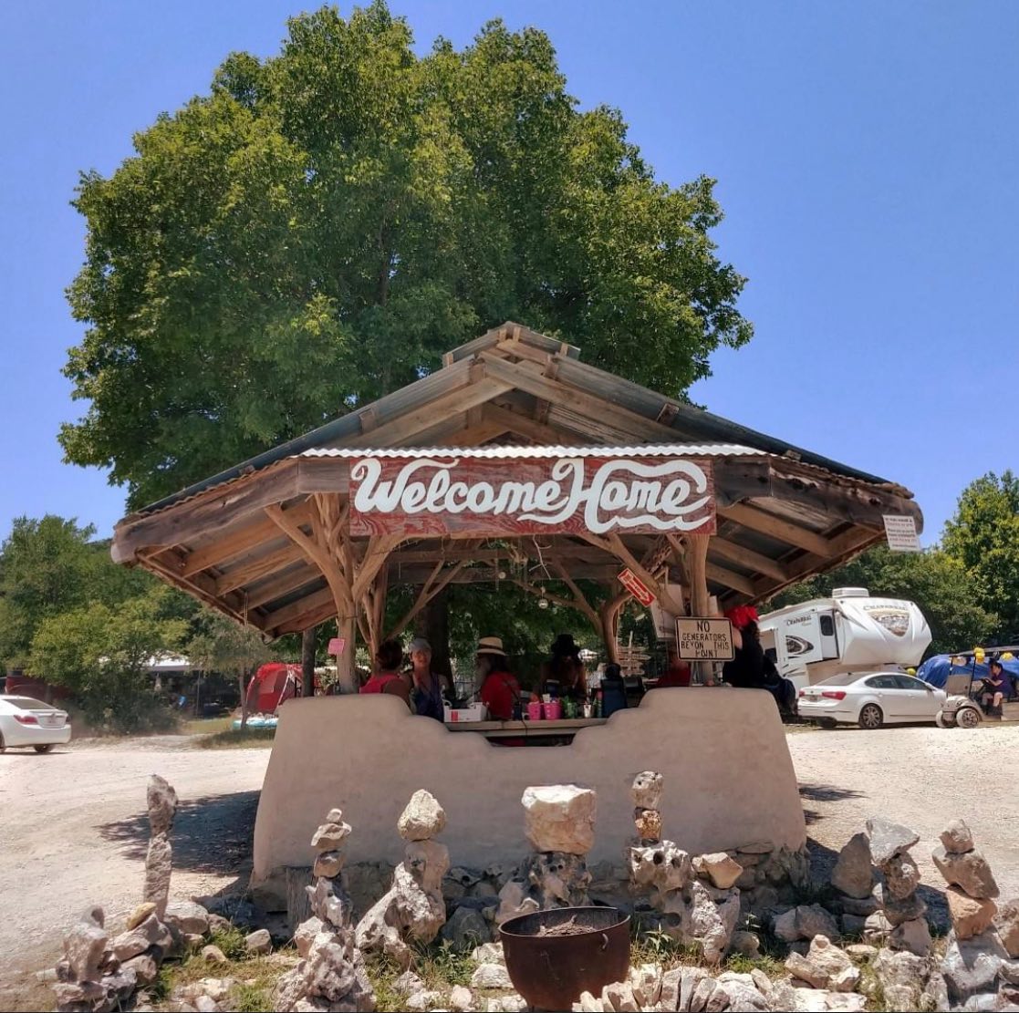 The "Welcome Home" entrance kiosk at the Kerrville Folk Festival under a bright blue sky.