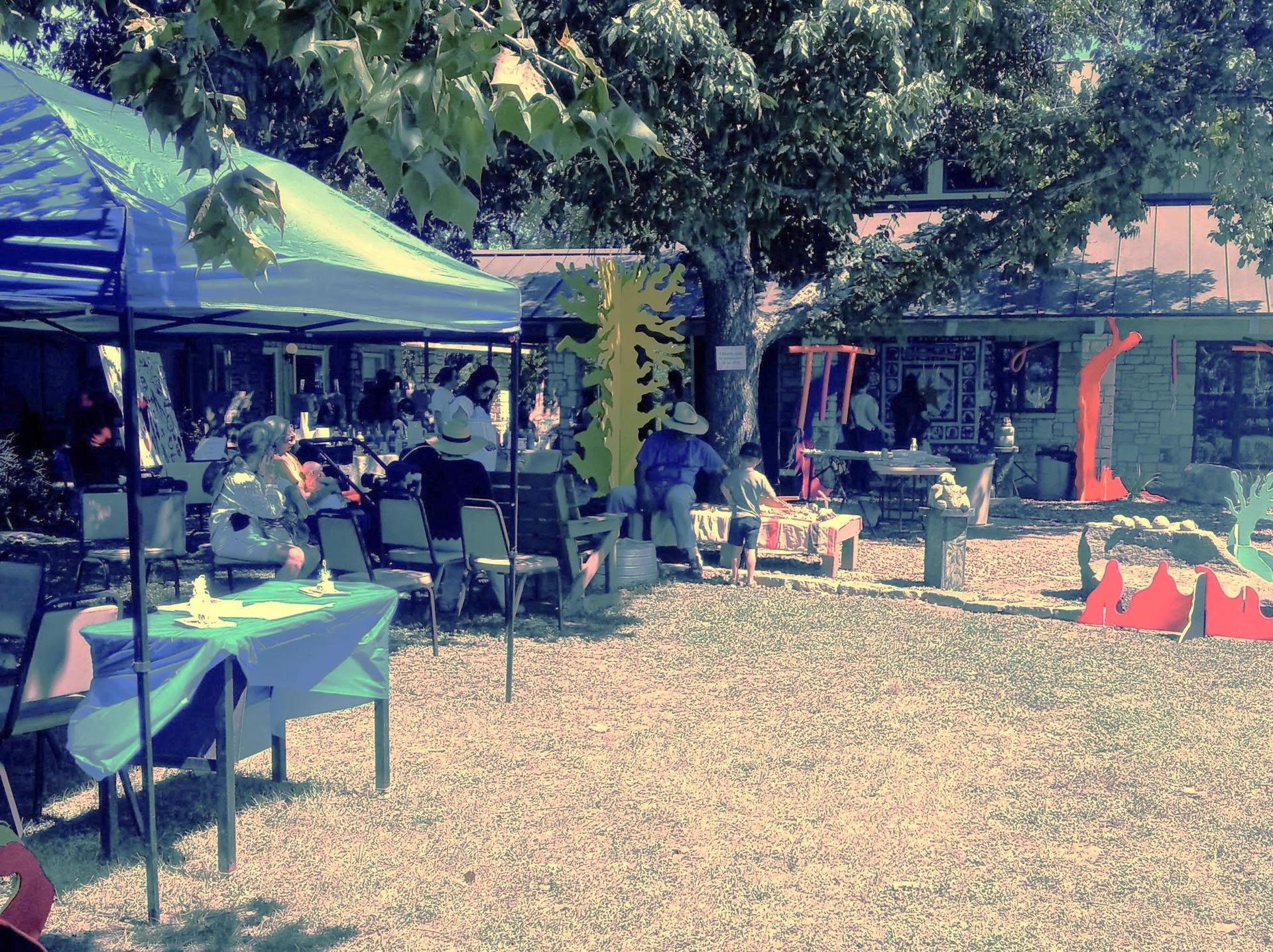 An outdoor event setup on a sunny day during the Family Art History Weekend, featuring tables and shade canopies on a grassy area.