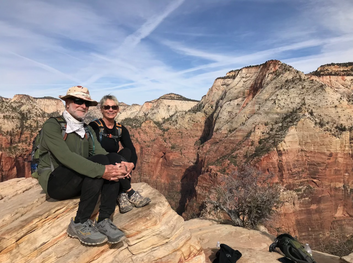 Musicians C&B Booker Duo smiling and sitting on a rocky ledge overlooking a desert canyon.