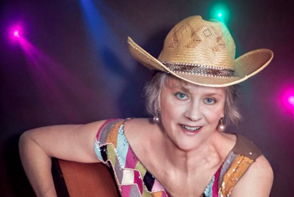 Musician Jerialice wearing a cowboy hat and smiling on stage under colorful concert lights.