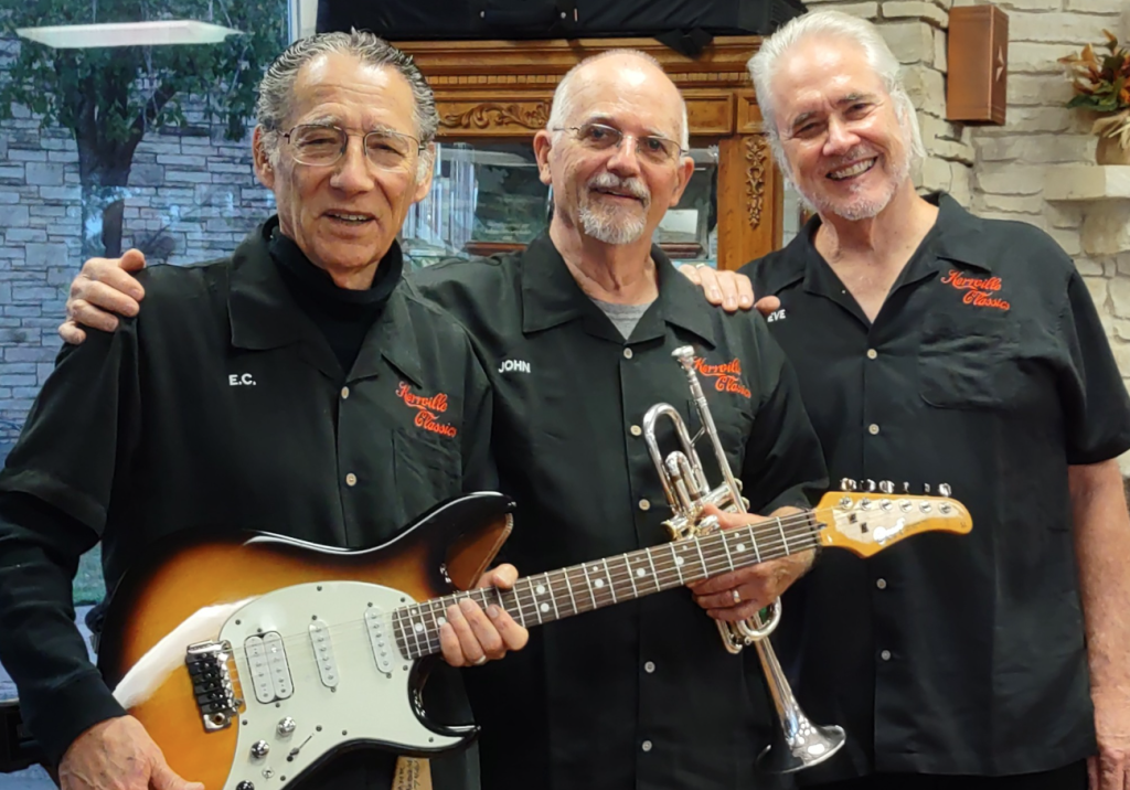Three members of the band Kerrville Classics smiling and holding an electric guitar and a trumpet.
